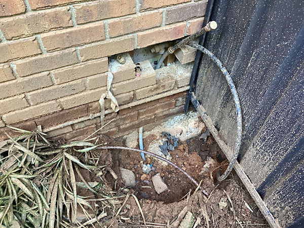 Unprotected leaking plastic water pipe passing through the brick wall in Jerrabomberra